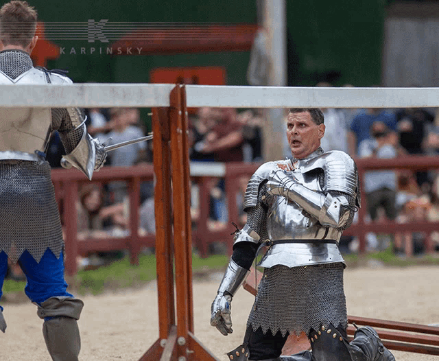 a man in a knight 's armor is kneeling down in front of a fence with karpinsky written on the top