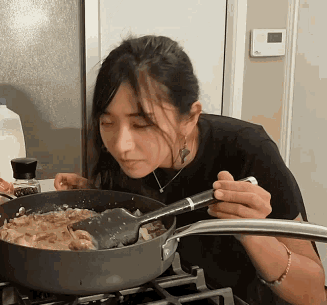 a woman is stirring a pot of food with a spatula and a bottle of black pepper on the counter