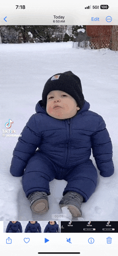 a baby is sitting in the snow and the time is 6:18