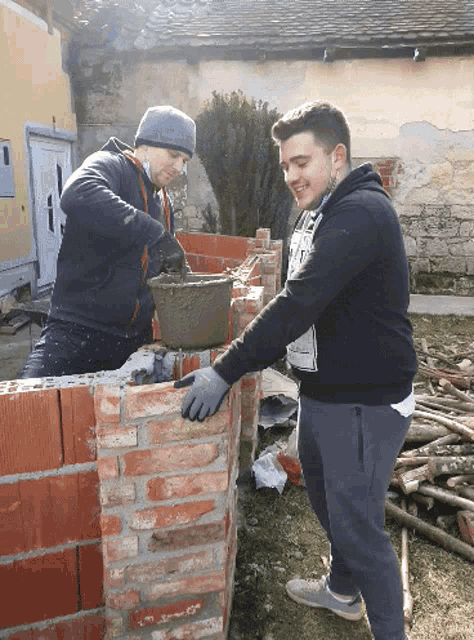 two men are working on a brick wall and one has a sweatshirt that says ' i love you ' on the back