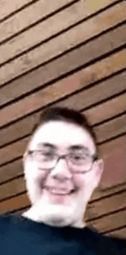 a man wearing glasses is smiling in front of a wooden ceiling .