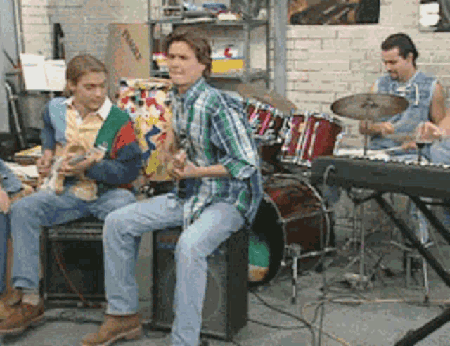 a group of young men are playing instruments in front of a drum set and a box that says fragile