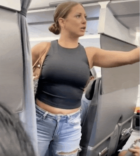 a woman in a black tank top and blue jeans is standing in a plane