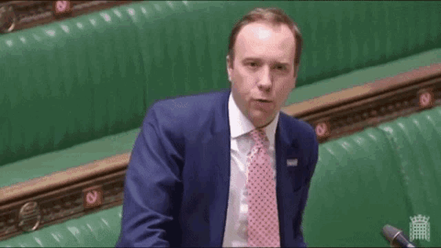 a man in a blue suit and pink tie is sitting in front of a microphone in a parliament .