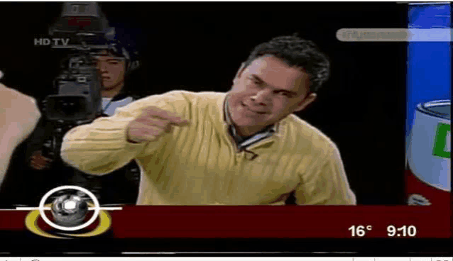 a man in a yellow sweater is pointing at the camera on a tv screen ..