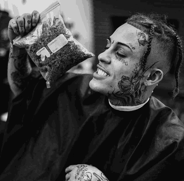 a man with a tattoo on his face is holding a bag of weed