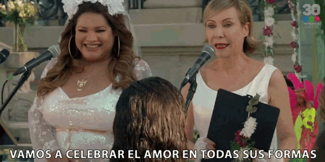 two women standing in front of microphones with the words " vamos a celebrar el amor en todas sus formas " below them