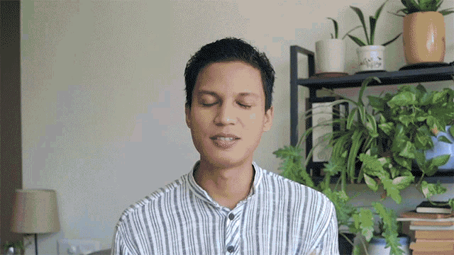 a man in a striped shirt with his eyes closed stands in front of a shelf full of potted plants