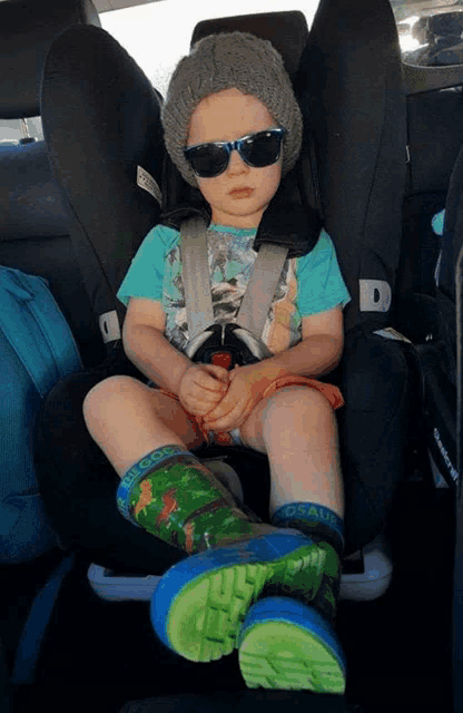 a little boy wearing sunglasses and a beanie is sitting in a car seat