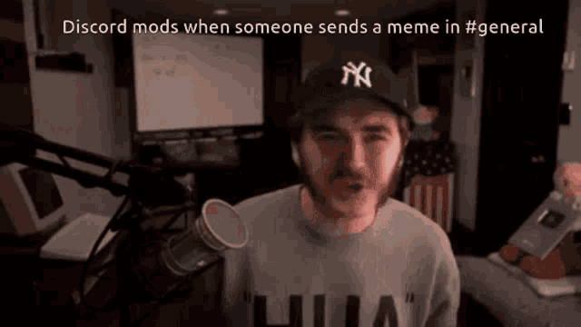 a man wearing a ny hat stands in front of a microphone and says discord mods when someone sends a meme