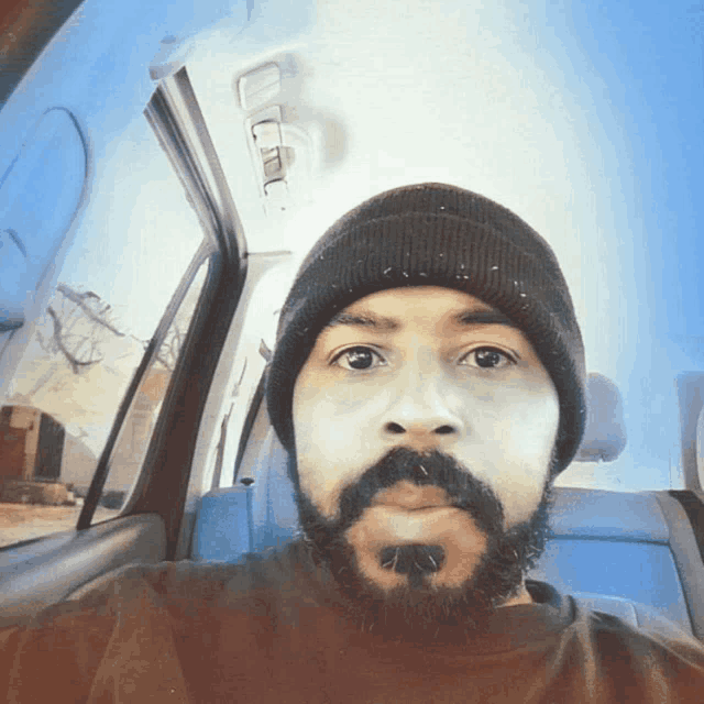 a man with a beard wearing a beanie takes a selfie