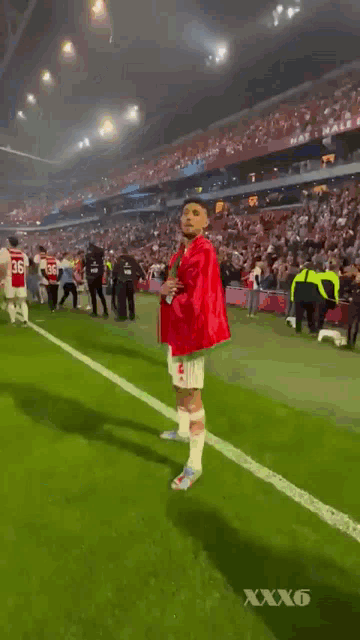 a man in a red and green shirt is walking on a soccer field with a crowd in the background .