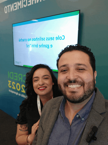 a man and a woman are posing for a picture in front of a tv screen that says ' a '