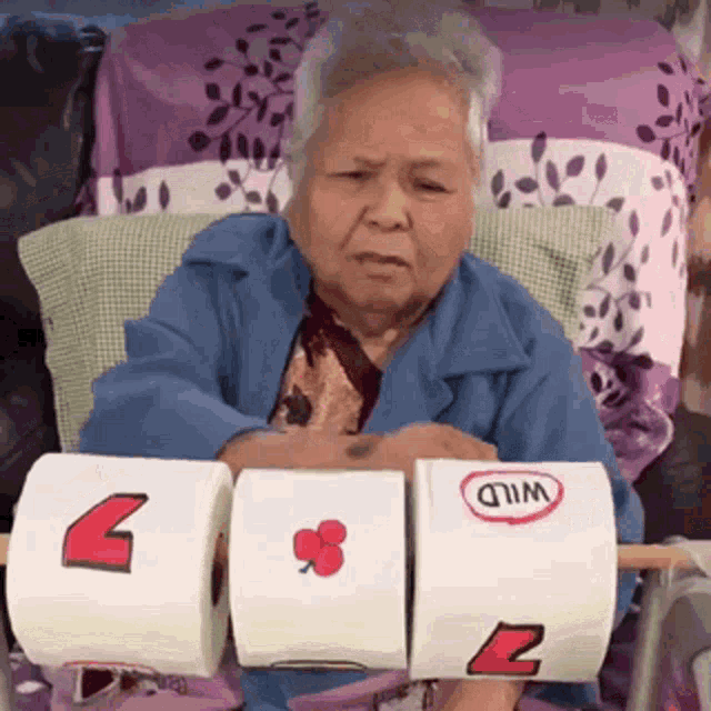 an elderly woman is sitting on a couch holding three rolls of toilet paper with wild written on them .