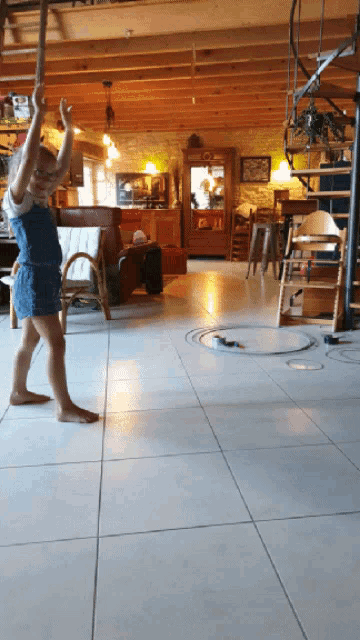 a little girl is standing on a tiled floor in a living room with a spiral staircase in the background