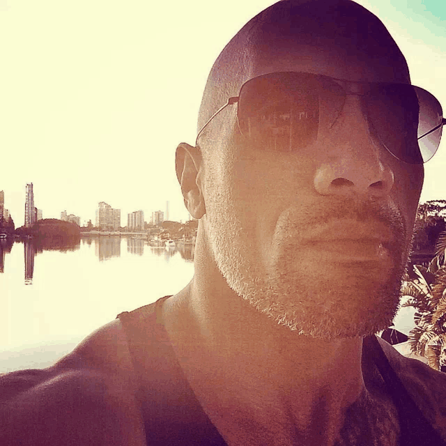 a man wearing sunglasses stands in front of a lake