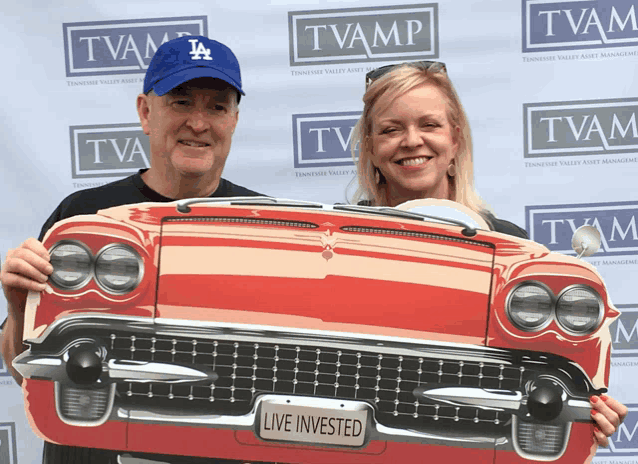 a man wearing a la dodgers hat is holding a red car with a live invested sign on it