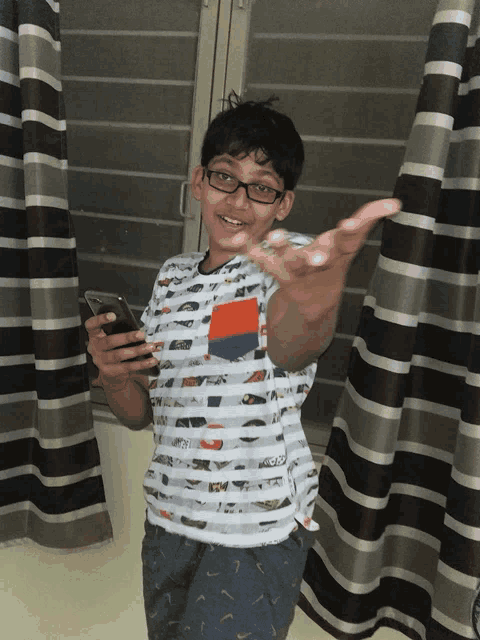 a boy wearing glasses and a striped shirt holds a cell phone in his hand