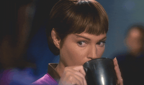 a woman in a purple shirt is drinking from a mug