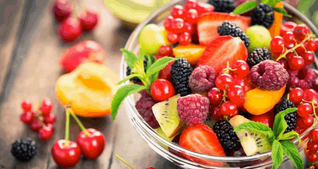 a bowl of fruit salad on a wooden table surrounded by other fruits .