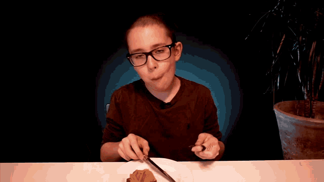 a young boy with glasses is sitting at a table with a plate of food and a knife and fork