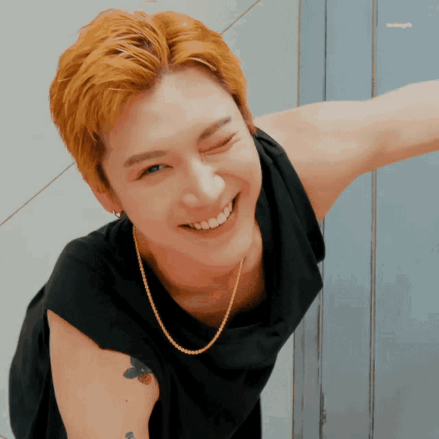 a young man wearing a black tank top and a gold chain smiles