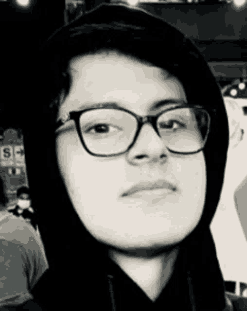 a young man wearing glasses and a black hoodie is looking at the camera .