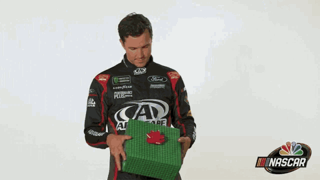 a man in a racing uniform is holding a green box and says merry christmas nascar .