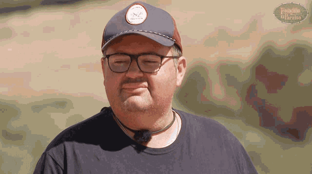 a man wearing glasses and a hat is standing in front of a field with a sign that says ' pueblo '