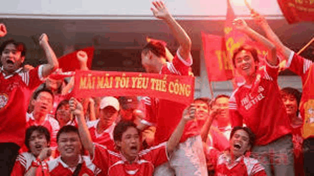 a group of people in red shirts are standing in a stadium holding flags .