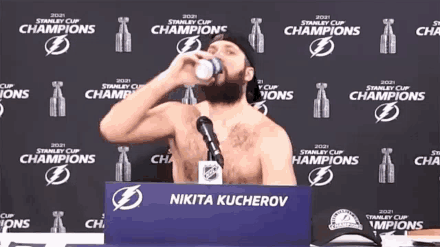 a shirtless man drinks from a bottle in front of a stanley cup champions banner