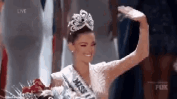 a woman wearing a crown and a miss universe sash is standing on a stage holding a bouquet of flowers .