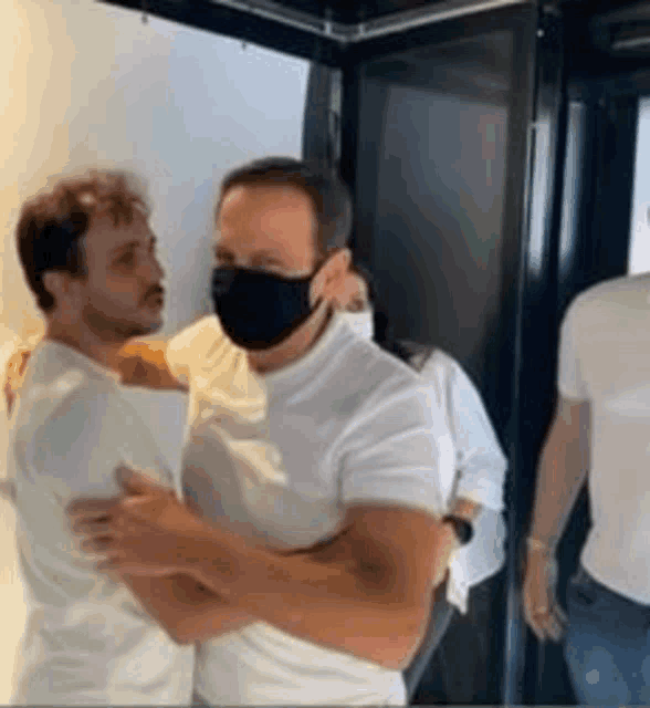 a man wearing a face mask is hugging another man .