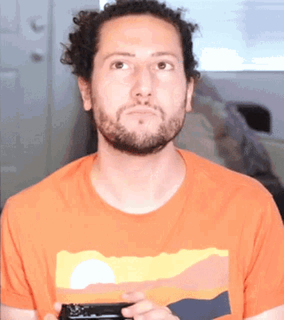 a man with a beard wearing an orange t-shirt with a sunset on it