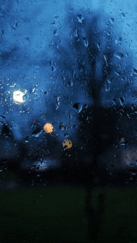 a window with a lot of rain drops on it and a light in the background