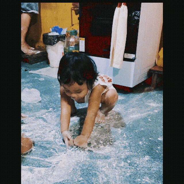 a little girl wearing a shirt that says ' coca cola ' on it is playing with flour on the floor