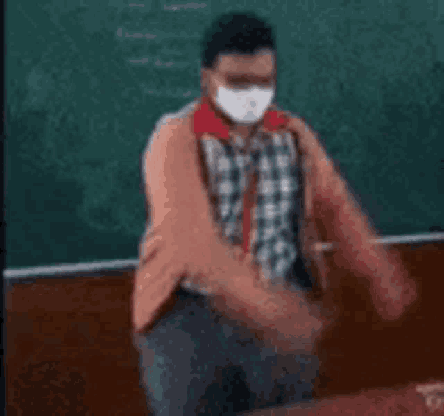 a man wearing a face mask is standing in front of a blackboard .