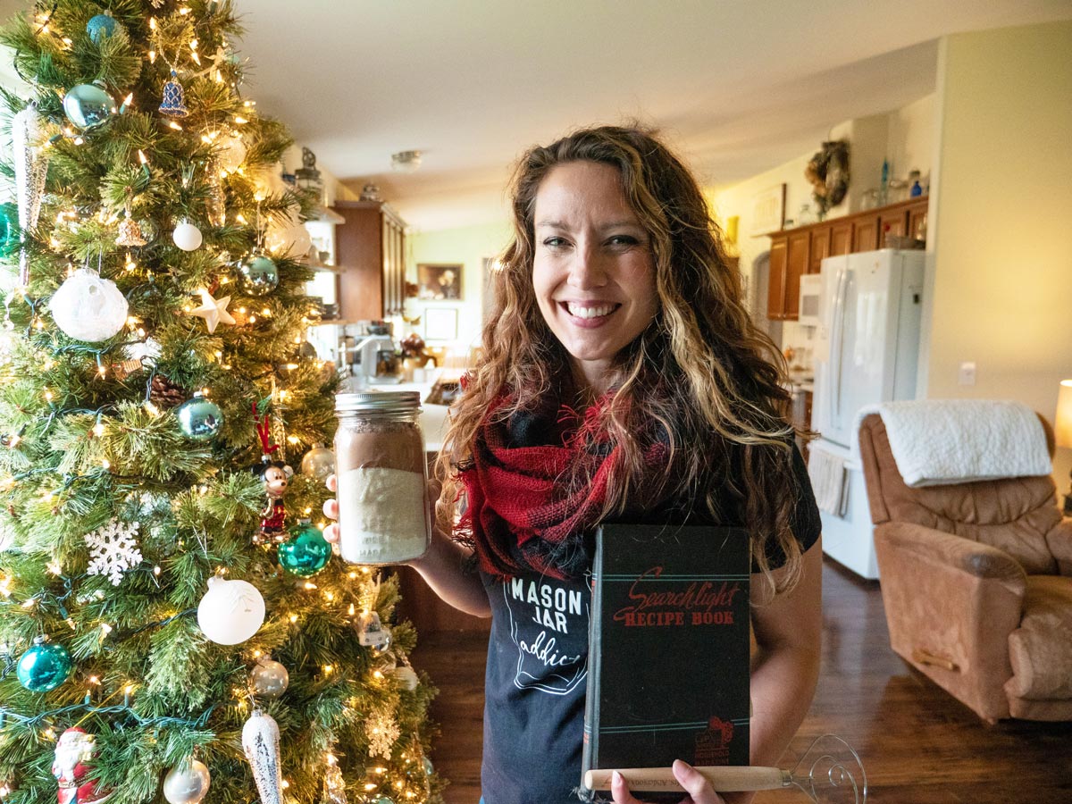 A woman standing by a Christmas tree holding up gifts.