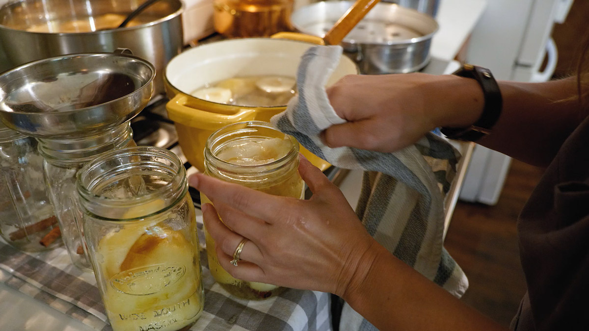 A woman wiping the rim clean of a jar of pears.