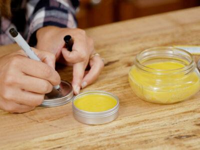 A woman labeling a tin of homemade healing salve.