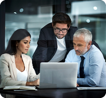 Three employees looking at a laptop computer at a desk