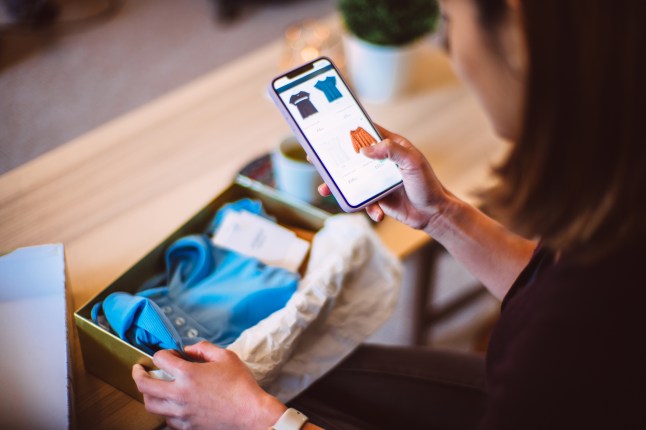 Young woman doing online shopping for clothes on smartphone at home