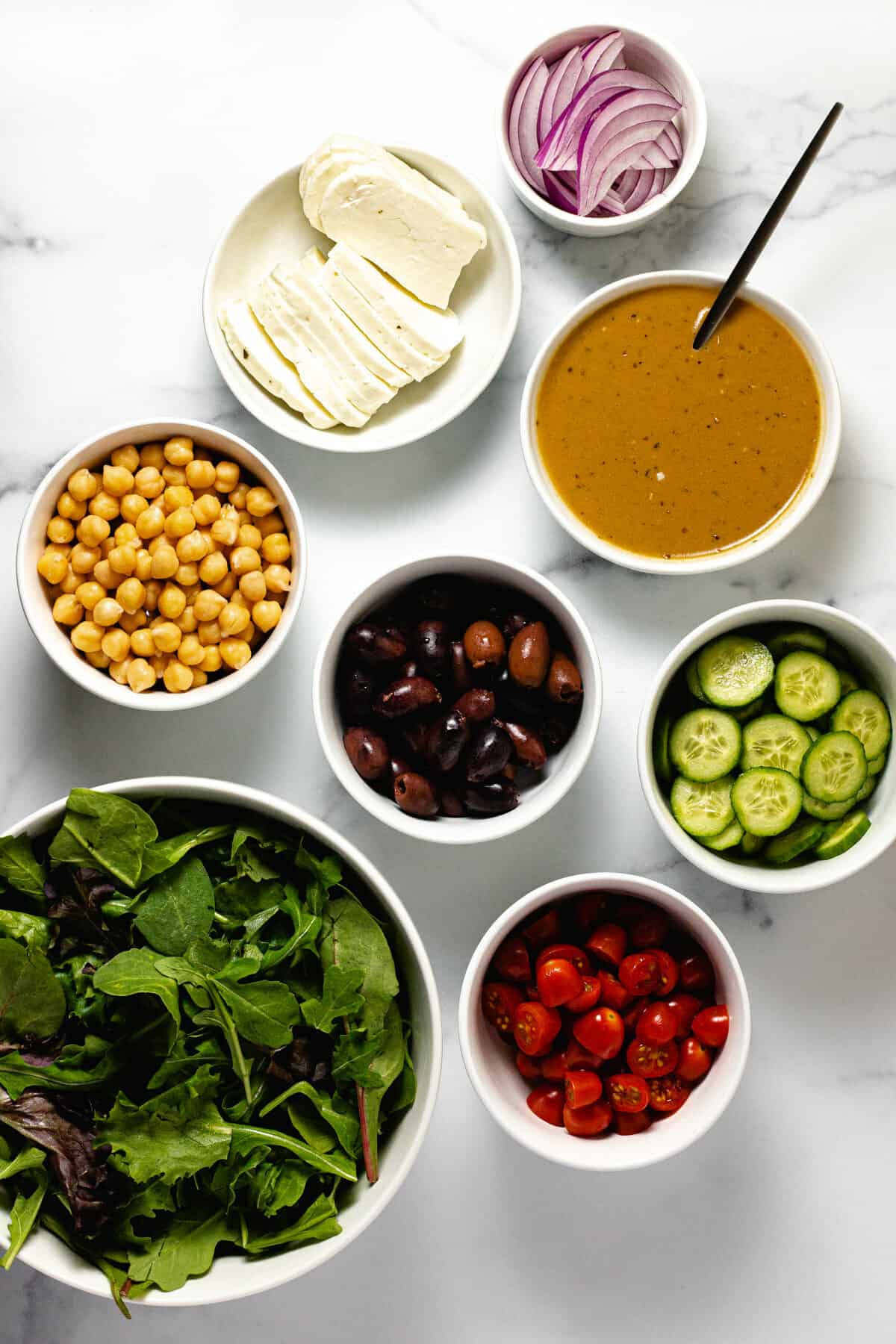 White marble countertop with bowls of ingredients to make grilled halloumi cheese salad