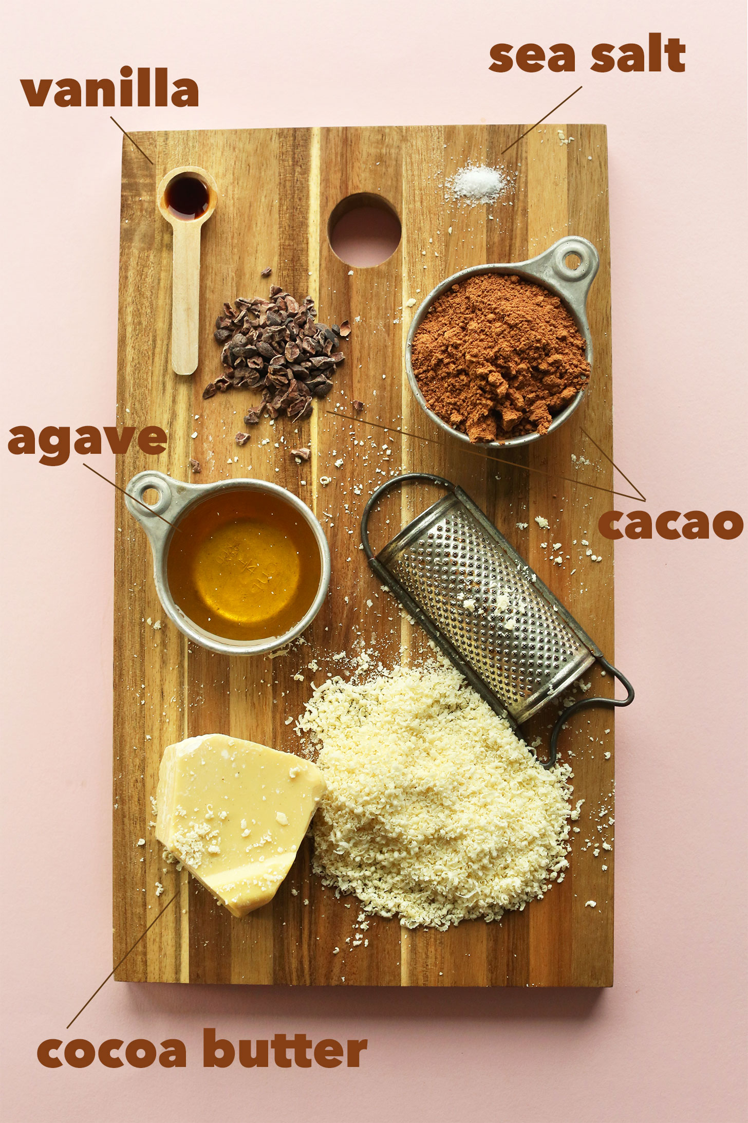 Cutting board with vanilla, agave, cocoa butter, cacao, and sea salt for making easy homemade vegan chocolate