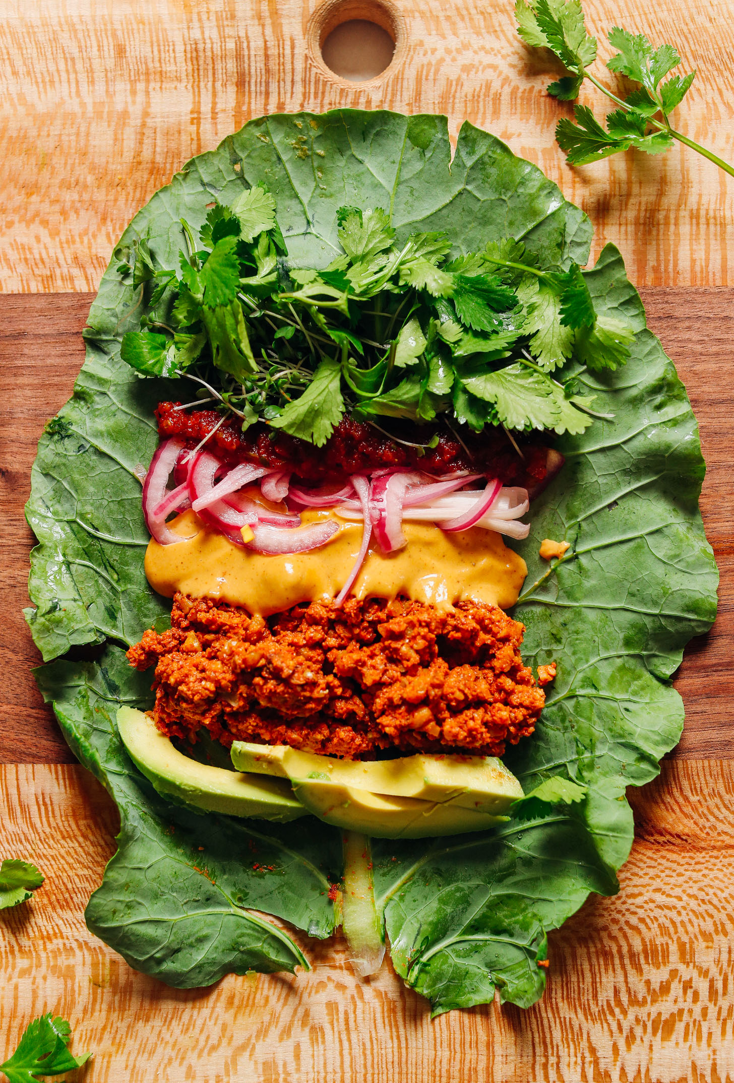 Wood cutting board with a collard green leaf topped with Mexican-inspired ingredients for Raw Vegan Burritos