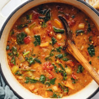 Using a wooden spoon to stir a pot of tuscan white bean and kale soup