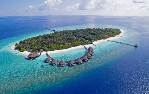 Aerial view of a tropical island with overwater bungalows and lush greenery surrounded by a coral reef. Adaaran Select Meedhupparu Maldives