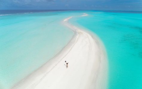 Person walking on a narrow sandbar surrounded by turquoise waters. Maldives.