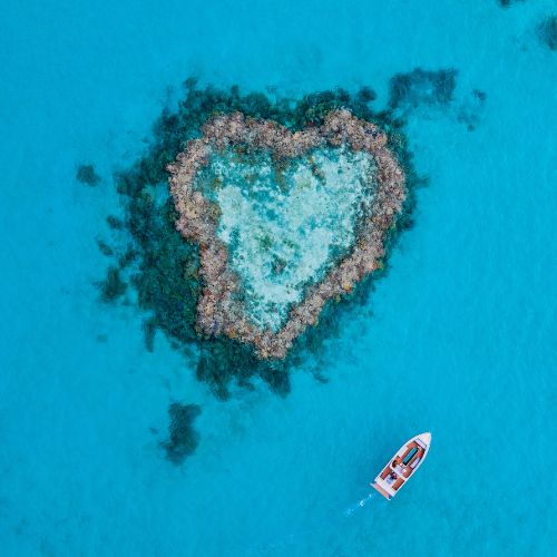 Aerial view of a heart-shaped reef with a boat nearby in a blue sea in Australia