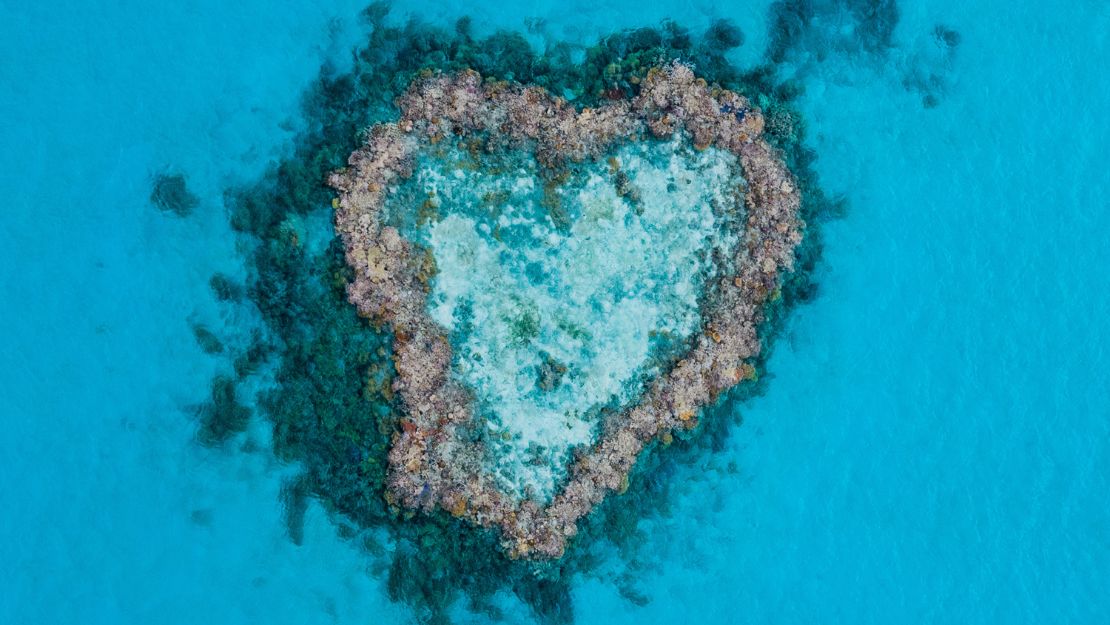 Aerial view of a heart-shaped reef with a boat nearby in a blue sea in Australia